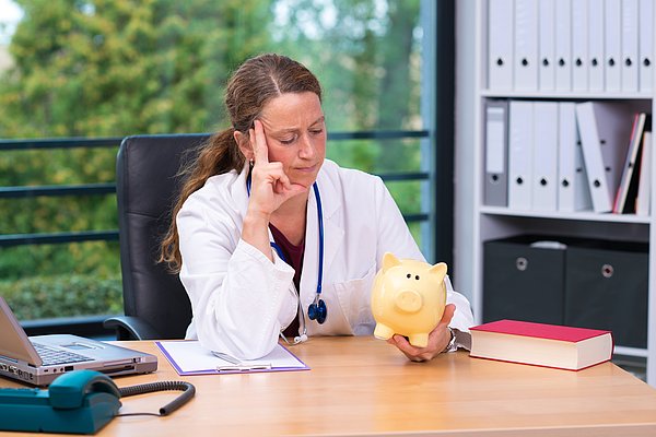 Ärztin sitzt verzweifelt vor ihrem Sparschwein
